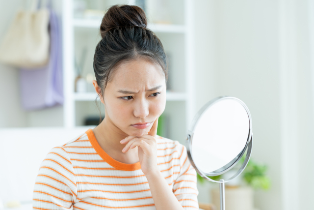 鏡を見て肌の状態に悩んでいる女性