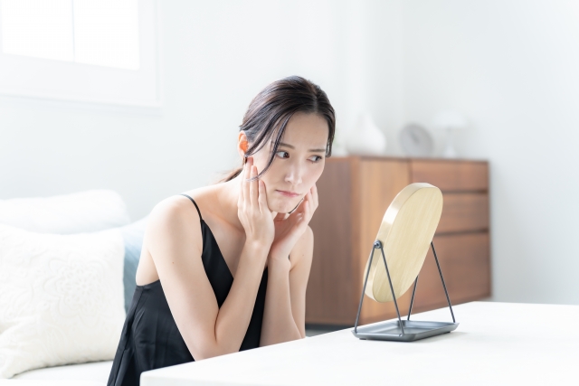 鏡をみて肌の状態に悩んでいる女性